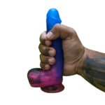 Mão masculina segurando o dildo cósmico azul e rosa com ventosa para demonstrar o tamanho real de 18 centímetros e a espessura